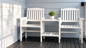 A patio with two white wooden chairs and a small table, a potted plant, and a wall-mounted device. - 2B at Swansea - cosy cottage, outdoor pet friendly (Swansea)