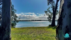 A lakeside view with trees framing the scene, a grassy area, and a clear sky. - Lake Sabai - Waterfront and private pool (Nords Wharf)