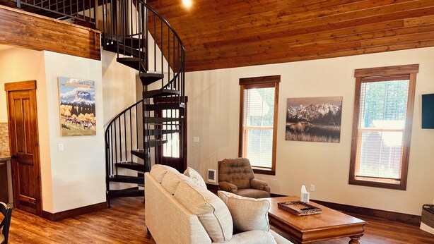 Ein Wohnzimmer mit Wendeltreppe, Holzboden, einer Couch, einem Sessel und Bildern an den Wänden.