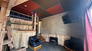 A wooden interior with a staircase, a black sofa, a small black cabinet, and a television on the wall.
