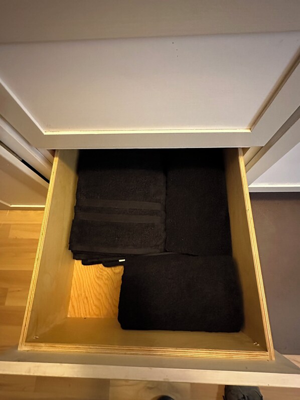 Un tiroir contenant des vêtements noirs pliés, un plancher en bois et un mur blanc.