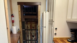 A narrow kitchen with wooden flooring, white cabinets, a wooden countertop, and a door leading to a wooden loft area.