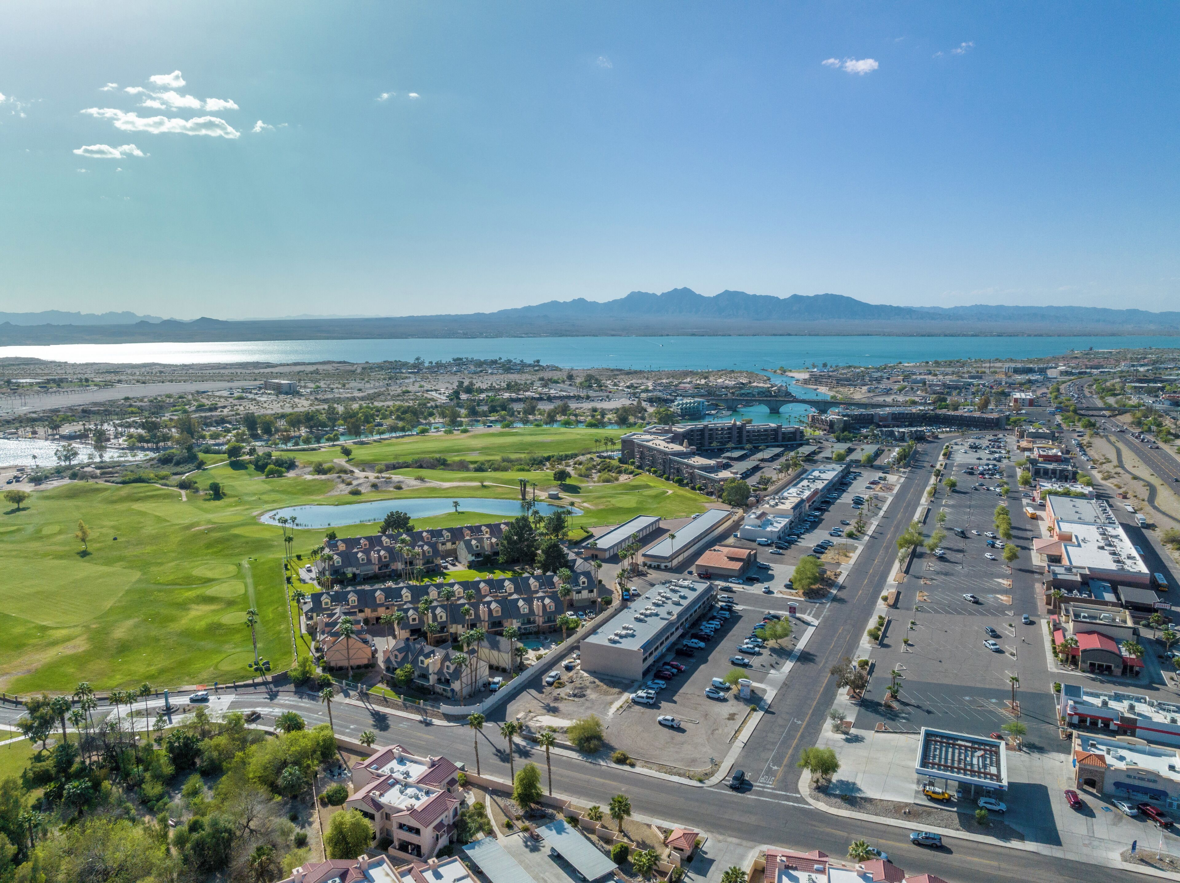A golf course with a large building complex, parking areas, and a view of the coastline.