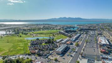 A golf course with a large building complex, parking areas, and a view of the coastline.
