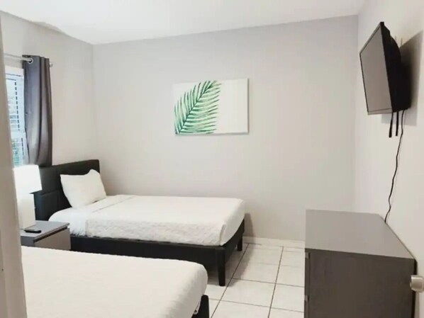 A hotel room with two beds, a flat-screen TV mounted on the wall, and a window with curtains.