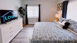 A bedroom with a bed, a TV, a dresser, a window with curtains, and a ceiling fan.
