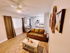 Un salon avec un canapé marron, une table basse ornée d’une plante et un ventilateur de plafond.