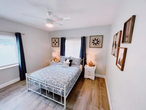 Ein Schlafzimmer mit Bett, Nachttischen, Deckenventilator und Wandbildern.