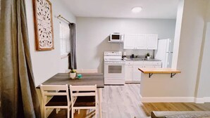 A compact kitchen with white cabinets, a microwave, and a stove. There is a dining table with chairs and a small plant on it.
