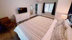 Une chambre à coucher avec un grand lit, un téléviseur posé sur une commode, une chaise et un ventilateur de plafond.