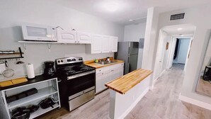 Une cuisine de taille réduite avec des meubles blancs, une cuisinière noire et un plan de travail en bois.