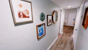 Un couloir doté d’un plancher en bois, de murs blancs et de plusieurs œuvres d’art encadrées.
