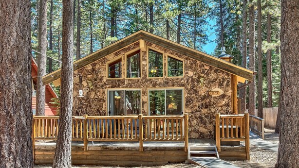Un chalet rustique avec une façade en pierre, de grandes fenêtres et une terrasse en bois.
