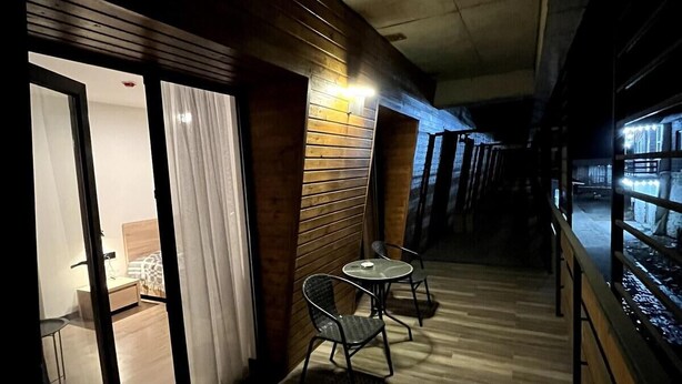 Ein Korridor mit Holzboden, eine Glastür zu einem Zimmer mit Bett und Tisch, und zwei Stühle in der Nähe der Tür.