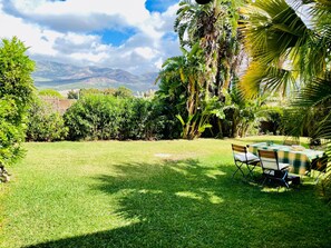 A well-maintained grassy backyard with a table and chairs, surrounded by lush tropical plants and a view of distant mountains. - Las Palomas Coastal Retreat, Tarifa sleeps 2-4 (Tarifa)