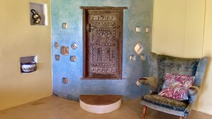 Een kamer met een blauwe accentmuur, een houten deur met ingewikkelde houtsnijwerken, een klein plankje met decoratieve objecten, en een gestreept fauteuil.