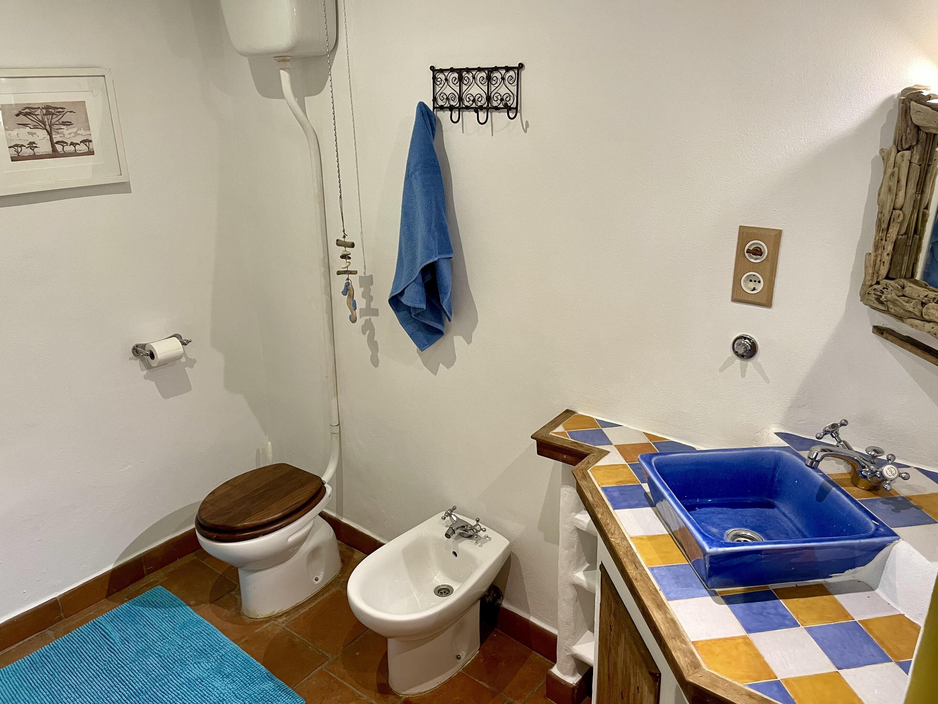 A bathroom with a toilet, bidet, sink, and a blue towel hanging on the wall.