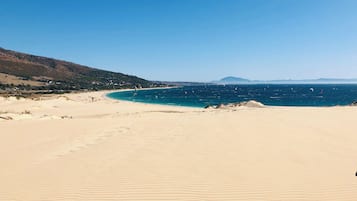 Un'ampia spiaggia sabbiosa con un mare cristallino e montagne sullo sfondo.