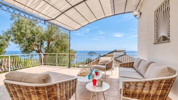 Un'area relax all'aperto con mobili in vimini, un tavolino con delle tazze e vista sul mare.