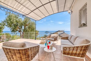 A covered outdoor seating area with wicker furniture, a small table with cups, and a view of the sea. - Villa Luce del Sol with Pool - L, Alassio, Italy (Alassio)
