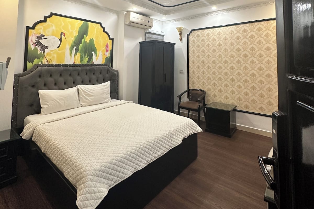 A bedroom with a bed, a chair, an air conditioning unit, and a decorative wall.