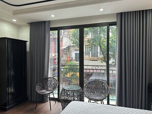 Hotellihuone, jossa on suuri ikkuna, sänky, kaksi rottinkituolia ja musta vaatekaappi.