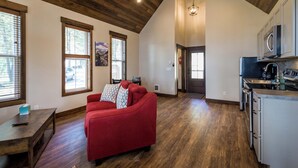 A spacious living area with a red sofa, wooden flooring, and a kitchen with modern appliances.