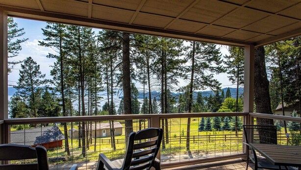 A covered porch with a view of a forest and a lake.