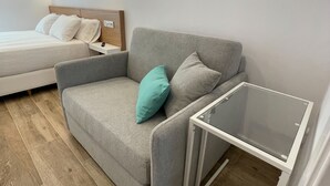 Een moderne slaapkamer met een grijze bank, een klein tafeltje en een bed met wit beddengoed.