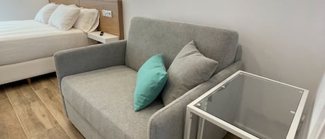 Een moderne slaapkamer met een grijze bank, een klein tafeltje en een bed met wit beddengoed.