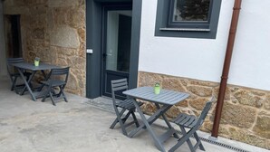 Een terras met twee tafels, vier stoelen, een stenen muur en een deur met een raam erboven.