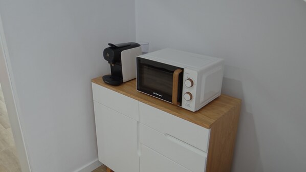 A microwave oven on a wooden cabinet with a coffee maker beside it.