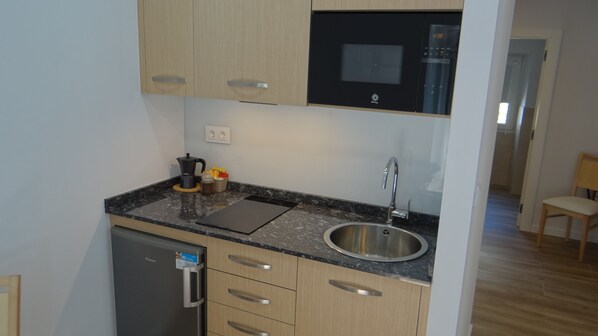 Una cocina compacta con refrigerador, microondas, pileta y armarios de madera.