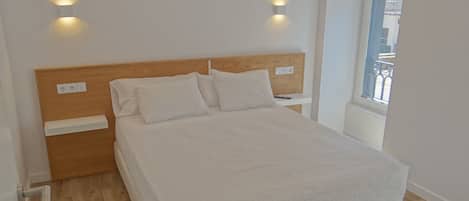 A neatly made bed with a wooden headboard, two bedside tables, and a window with a view.