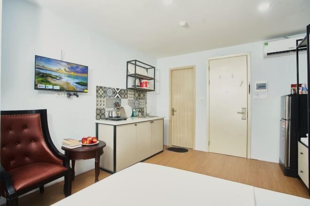 Ein kleiner Raum mit einem Bett, einem Tisch mit Äpfeln, einem Stuhl, einem Fernseher, einem Schrank und einer Tür.