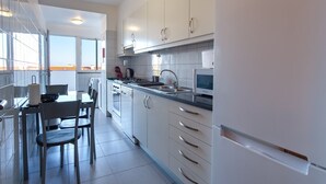 A modern kitchen with white cabinets, a stove, and a sink. There is a dining area with chairs and a table. - GuestReady - Grandiose Getaway in Caniço (Caniço)