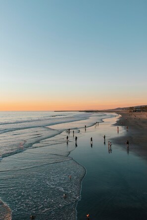A beach with people walking along the shore and a calm sea.