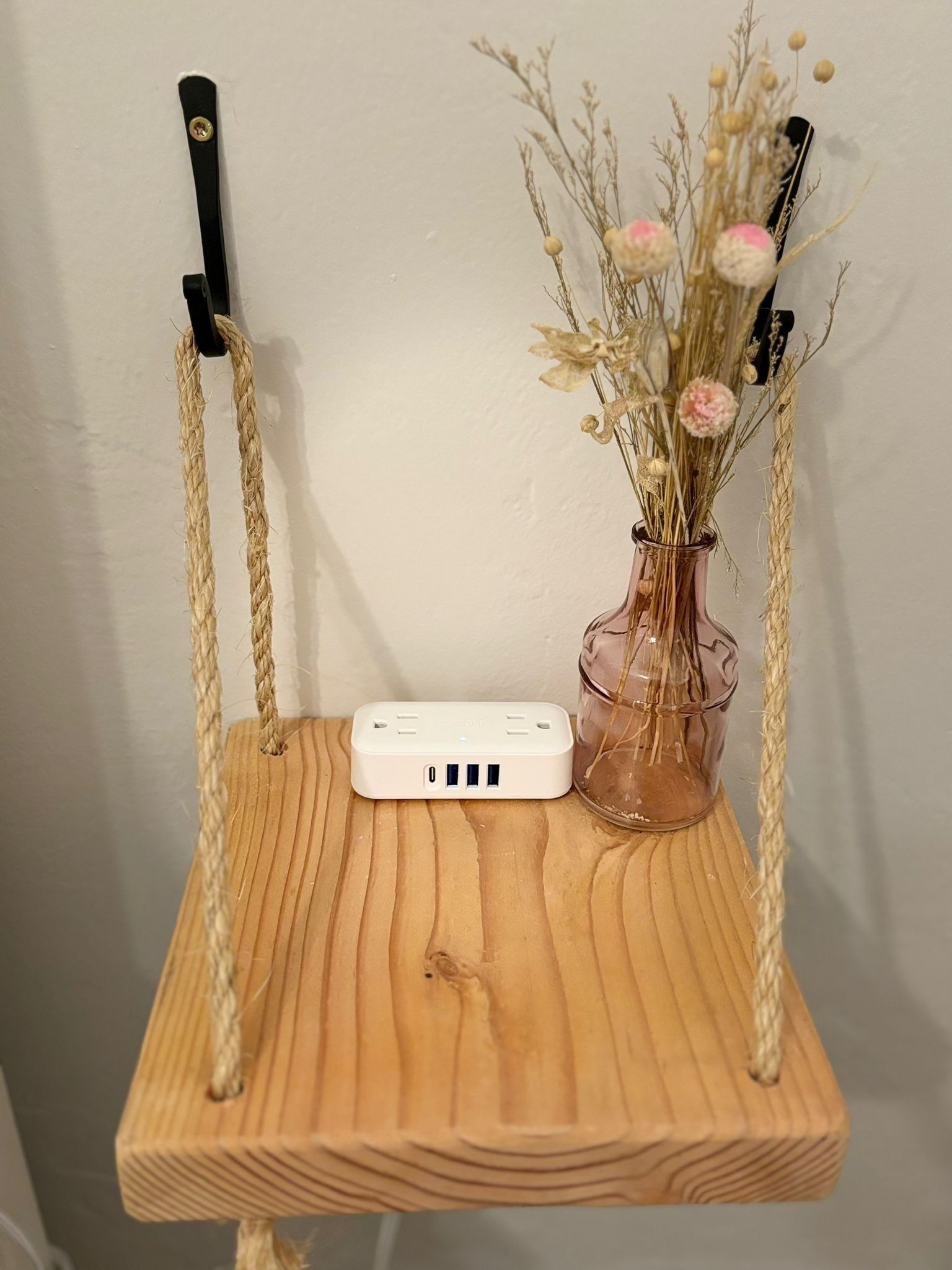 Ein Schaukelstuhl aus Holz mit einer weißen Vorrichtung darauf, eine Vase mit getrockneten Blumen und ein Seil.