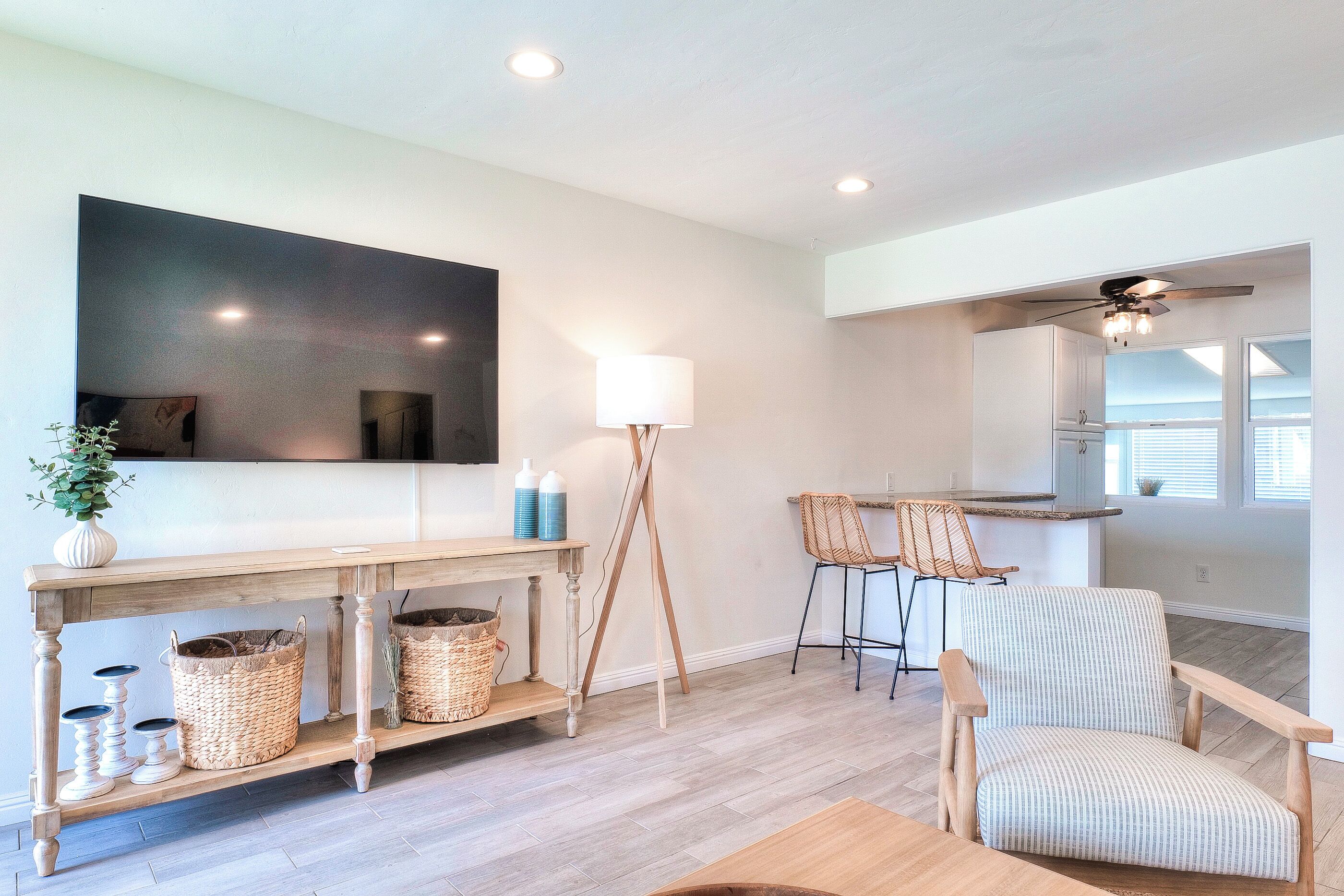 A modern living room with a wooden console table, wicker baskets, a large flat-screen TV, and a ceiling fan.