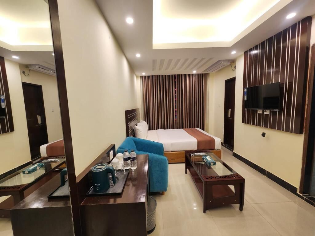 Une chambre d’hôtel avec un lit, un canapé bleu, une table basse, un téléviseur fixé au mur et une fenêtre avec des rideaux.