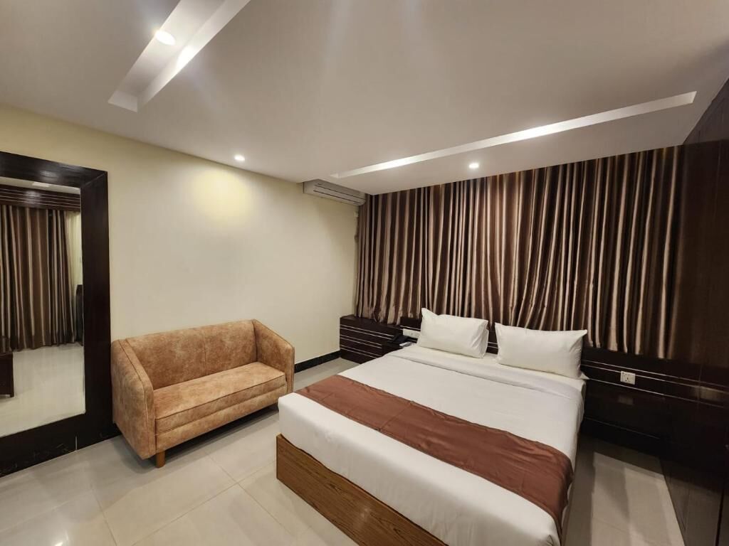 A modern hotel room with a large bed, a sofa, a nightstand, and a mirror.