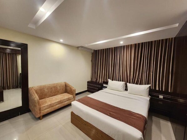 Una habitación de hotel moderna con una cama grande, un sofá, una mesita de noche y un espejo.