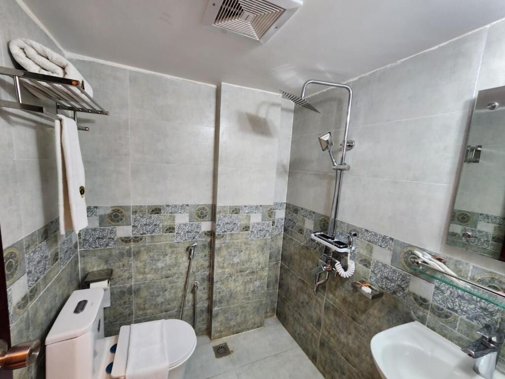 Ein Badezimmer mit Dusche, Toilette und Waschbecken, mit Fliesenwänden und einer Glasablage.