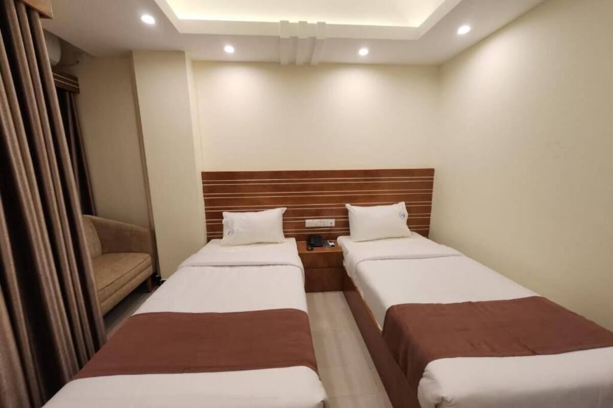 A hotel room with two single beds, a wooden headboard, a nightstand, and a sofa.