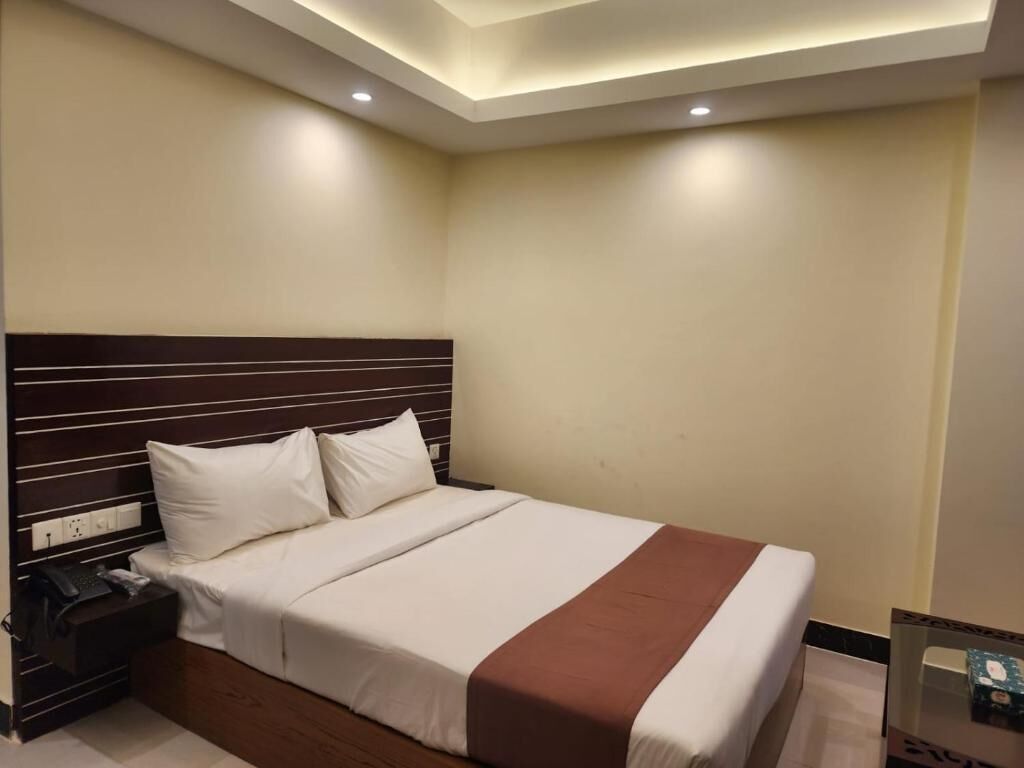 A hotel room with a large bed, a wooden headboard, a nightstand with a phone, and a small table with a box.