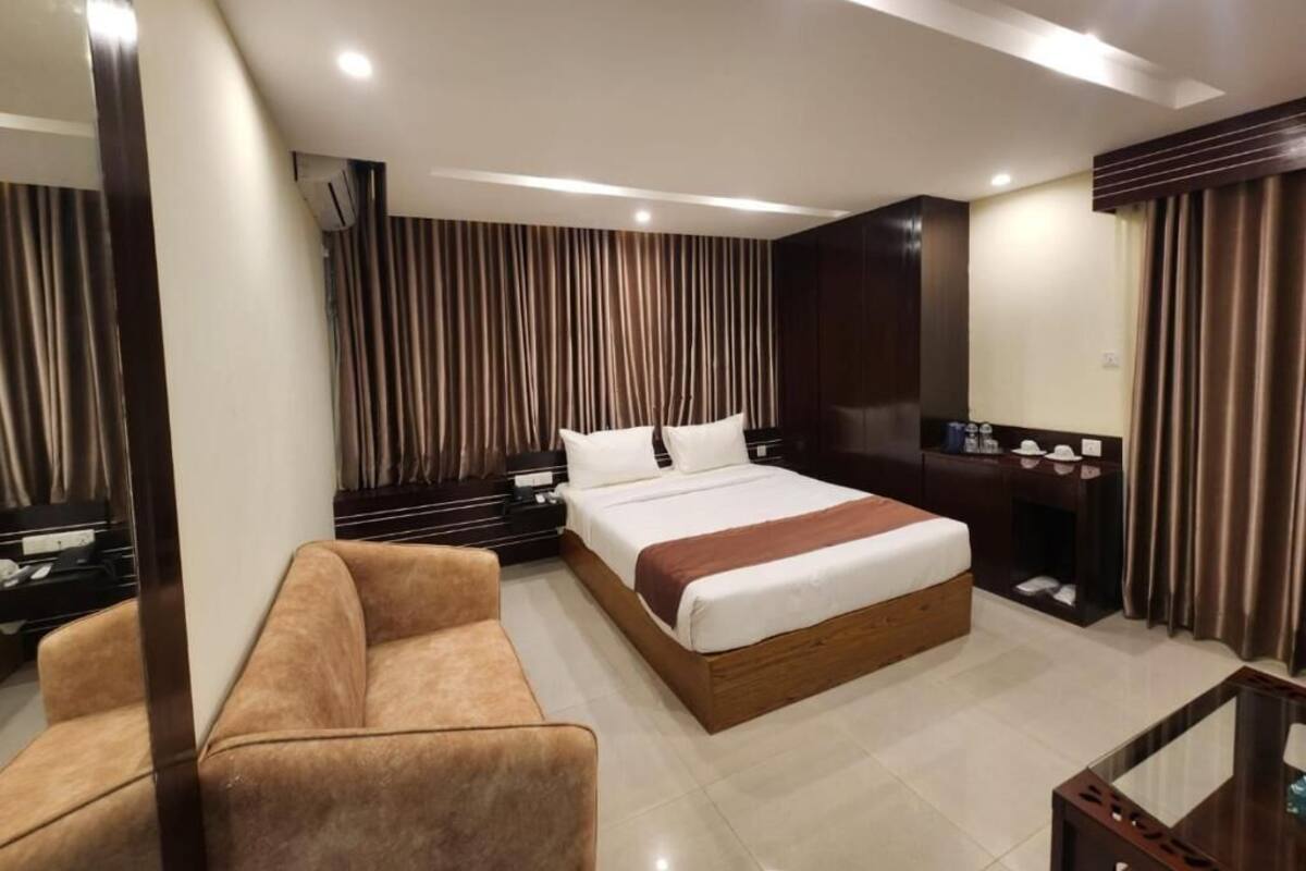 A hotel room with a large bed, a sofa, a desk, and a mirror.