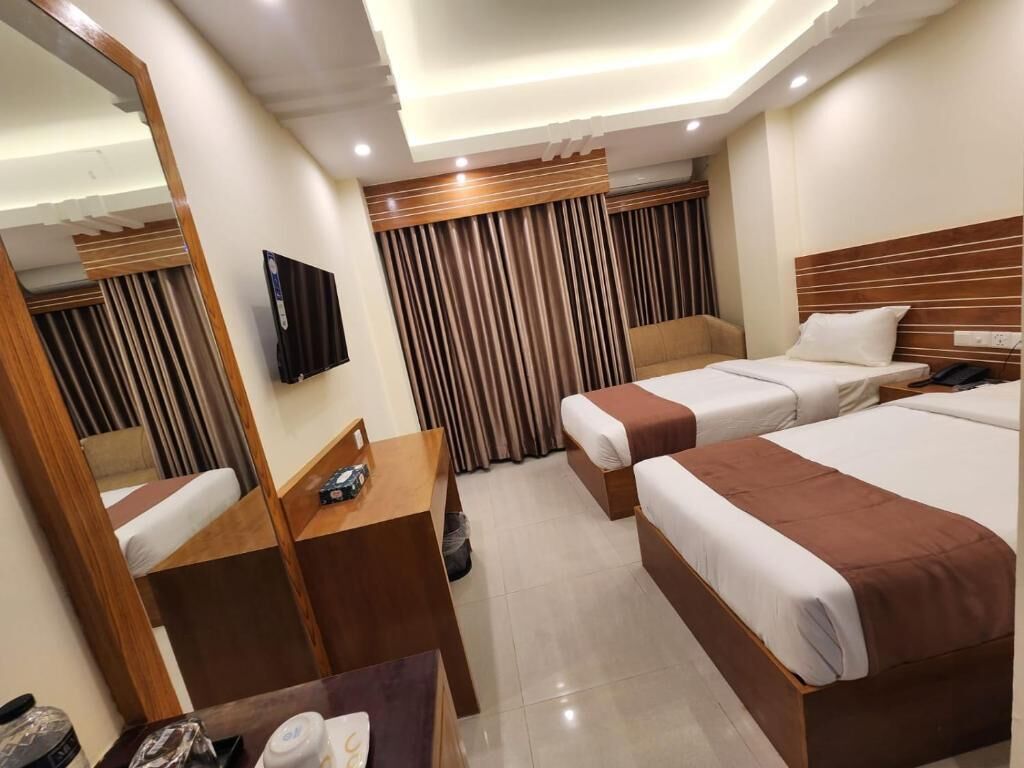 A hotel room with two beds, a desk, a chair, a TV, and a mirror.