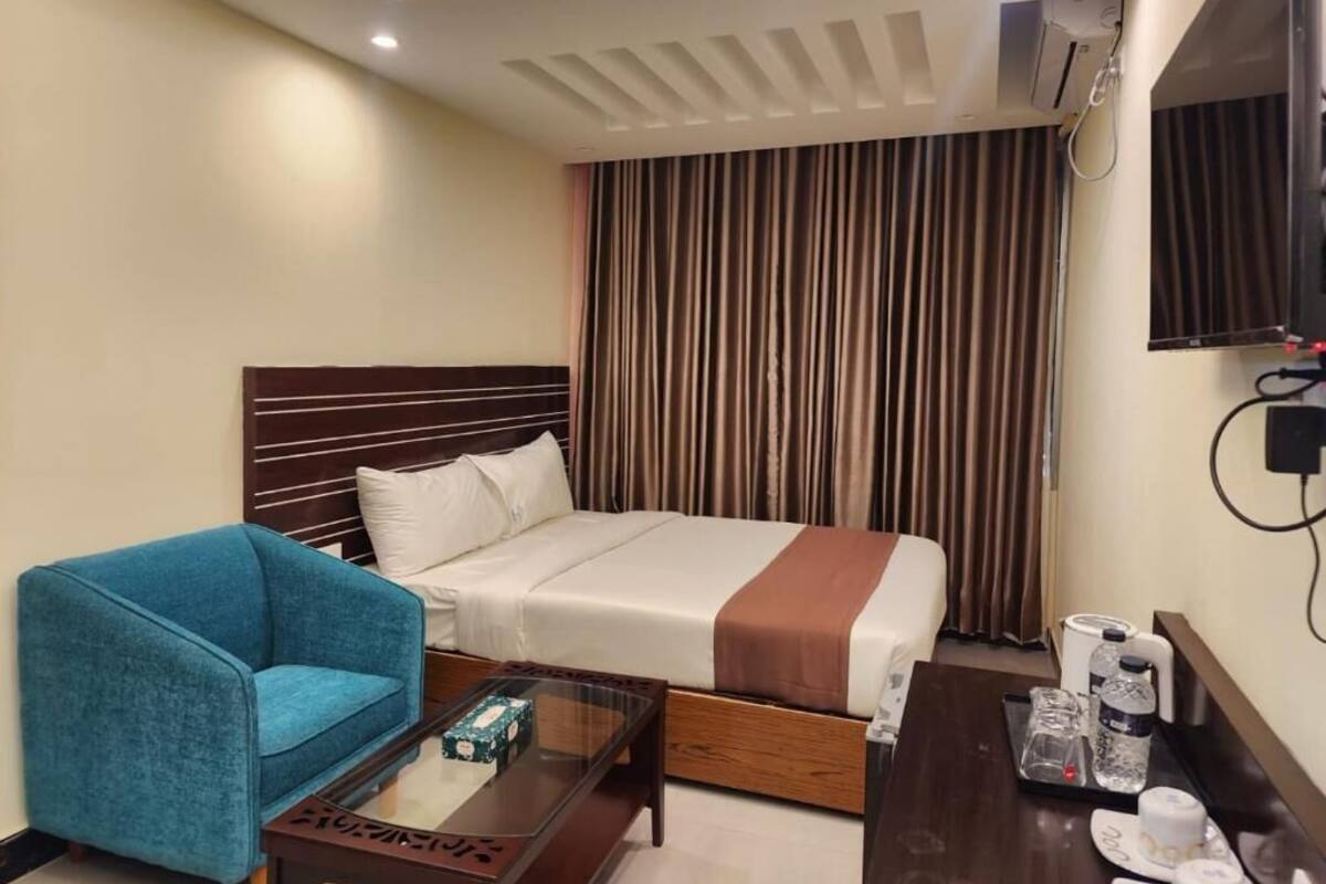 A hotel room with a bed, a blue armchair, a wooden coffee table, and a TV mounted on the wall.