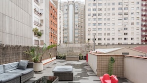 A rooftop terrace with a sofa, ottoman, and a red rocking chair. - Eixample 3BD Apartment with Private Terrace (Barcelona)