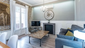 A living room with a brick wall, a large clock, a fireplace, and a television. - Eixample 3BD Apartment with Private Terrace (Barcelona)